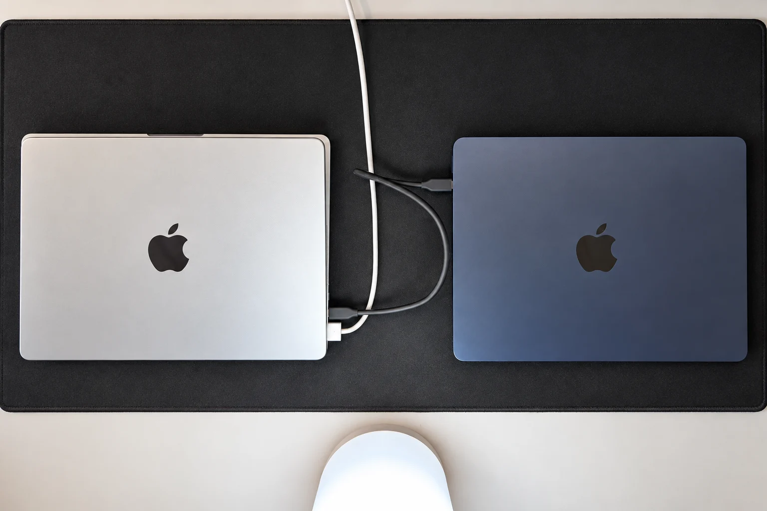 Dwa zamknięte MacBooki połączone przewodem USB-C na biurku.